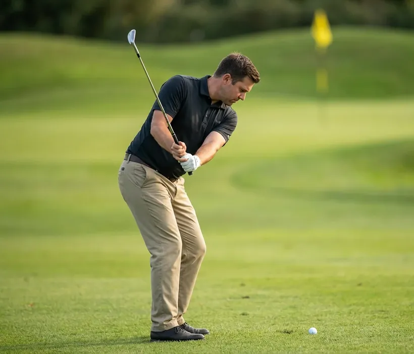 A golfer playing a short pitch shot towards the flag